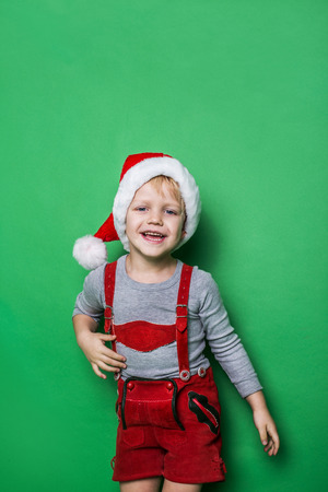 Little blond boy with Santa Claus cap smiling. Studio portrait over green backgroundの写真素材
