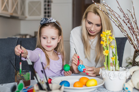 Mother And Daughter Painting Easter Eggs In Home. Girl with her mother learning to paint Easter eggs. Cozy home atmosphere. Easterの写真素材