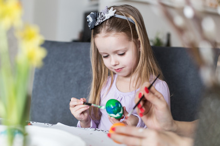Easter, family, holiday and child concept - close up of little girl and mother coloring eggs for easterの写真素材