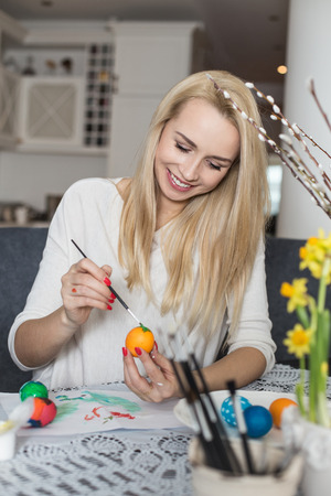 Beautiful young woman painting easter eggs. Cozy home atmosphere. Easterの写真素材