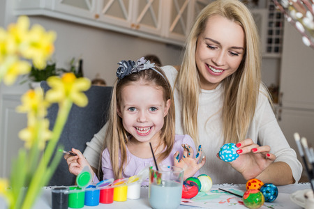 Happy mother and daughter painting easter eggs in the living room. Easter, family, holiday and child conceptの写真素材