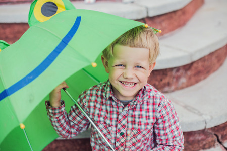 Adorable toddler boy with green frog umbrella. Outdoors portraitの写真素材