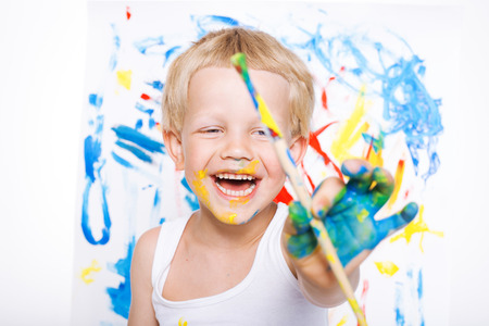 Little messy kid painting with paintbrush picture on easel. Education. Creativity. School. Preschool. Studio portrait over white backgroundの写真素材