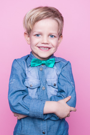 Young beautiful boy with blue shirt and butterfly tie. Studio portrait over pink backgroundの写真素材