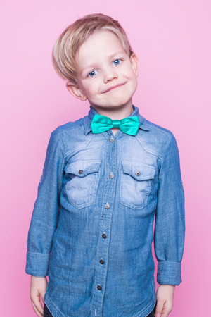 Young beautiful boy with blue shirt and butterfly tie. Studio portrait over pink backgroundの写真素材