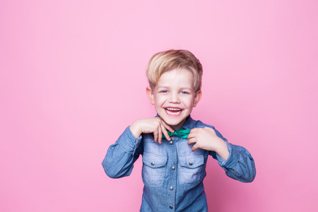 Young handsome kid smiling with blue shirt and butterfly tie. Studio portrait over pink backgroundの写真素材