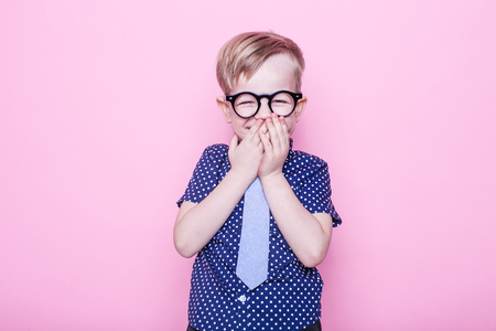 Little adorable kid in tie and glasses. School. Preschool. Fashion. Studio portrait over pink backgroundの写真素材