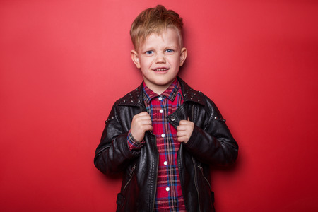 Fashionable child in leather jacket. Studio portrait over red backgroundの写真素材