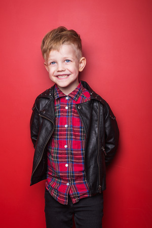 Fashion little boy wearing a leather jacket. Studio portrait over red backgroundの写真素材