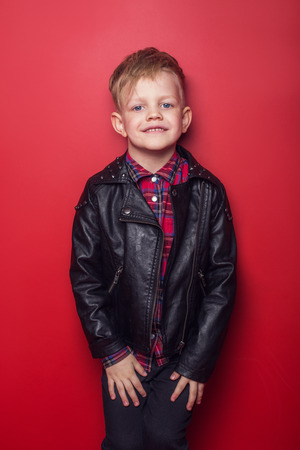 Fashion little boy wearing a leather jacket. Studio portrait over red backgroundの写真素材