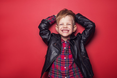 Fashion little boy wearing a leather jacket. Studio portrait over red backgroundの写真素材