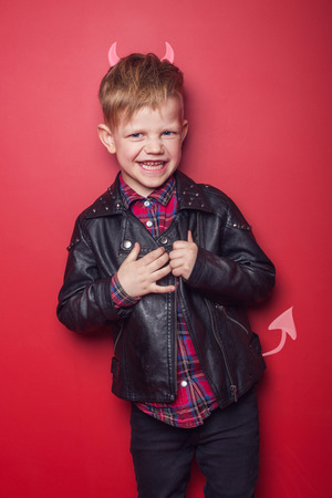 Little handsome devil with horns and tail. Kid. Halloween. Studio portrait isolated over red backgroundの写真素材