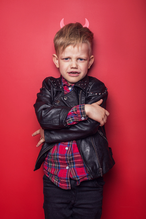Little handsome devil with horns and tail. Kid. Halloween. Studio portrait isolated over red backgroundの写真素材