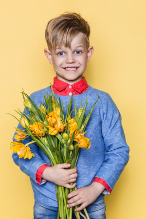 Little beautiful child with a bouquet of tulips. Son gives mom flowers on Women's Day, Mother's Day. Birthday. Valentine's day. Spring. Studio portrait over yellow backgroundの写真素材