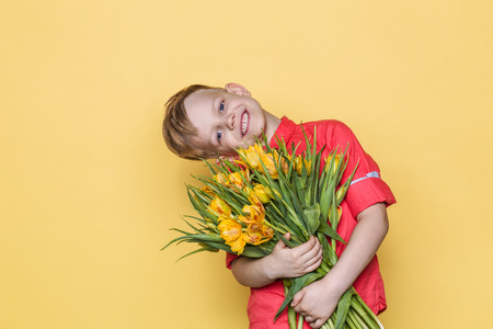 Little beautiful child with pink shirt gives a bouquet of tulips on Women's Day, Mother's Day. Birthday. Valentine's day. Spring. Studio portrait over yellow backgroundの写真素材