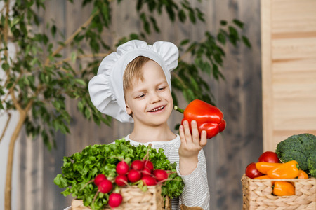 Handsome little kid in chef uniform with vegetables. Cooking in kitchen at home. Vegetarian. Healthy foodの写真素材