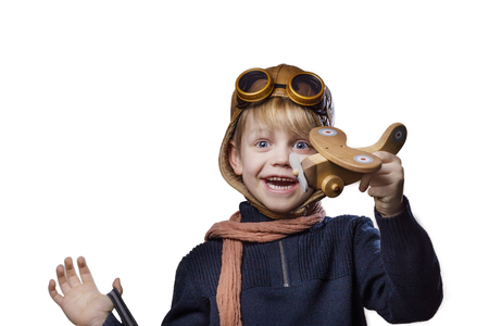 Happy child dressed in pilot hat and glasses. Kid playing with wooden toy airplane. Dream and freedom concept. Retro. Studio portrait isolated over white backgroundの写真素材