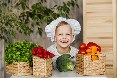 Handsome little kid in chef uniform with vegetables. Cooking in kitchen at home. Vegetarian. Healthy foodの写真素材