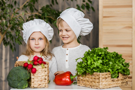 Handsome boy and beautiful young girl playing in the kitchen chefs. Healthy food. Vegetablesの写真素材