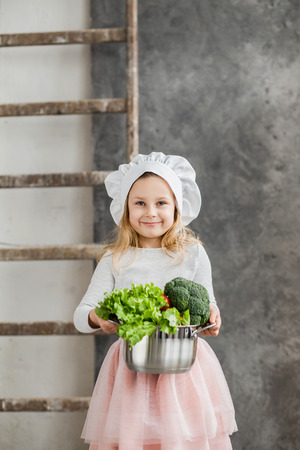 Little beautiful girl holding a pot full of vegetables. Healthy food. Harvest. Little housewifeの写真素材