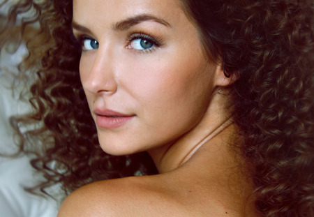 Portrait of a curly girl with blue eyes with bared shoulders sitting backの写真素材