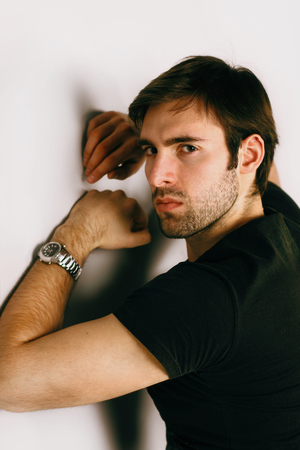 Fashion portrait of evil handsome smartlooking guy with Brown hair and Bright eyes in a black T-shirt and silver watch on his left hand is staring into the frame and looking angry was shooted From the Backの写真素材