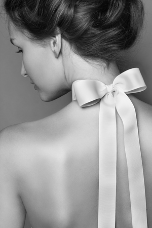Black and white tender fashion portrait of Beautiful gentle young brunette woman with silk bow on the neck, shooted from the Backの写真素材