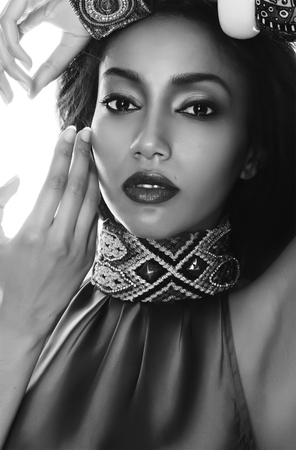 Black and white fashion portrait of the beautiful mulatto whith dark skin, hair and red lips in traditional ethnic accessories, and bracelet on her handの写真素材