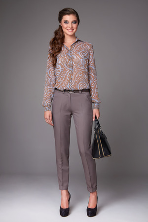 Beautiful sexy young business woman with evening make-up dressed in tight pants and silk blouse with lace long sleeves and high-heeled shoes and a small black handbag, business clothes for meetings and walksの写真素材