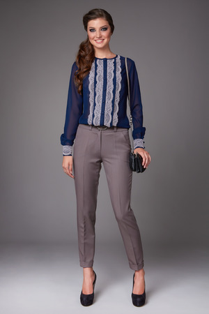 Beautiful sexy young business woman with evening make-up dressed in tight pants and silk blouse with lace long sleeves and high-heeled shoes and a small black handbag, business clothes for meetings and walksの写真素材