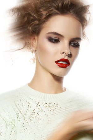 Beautiful young girl with a bright evening make-up, orange, scarlet lipstick, rosy cheeks, eye shadow, nail polish, blonde curly hair dressed in winter white knitted sweater holding a king chess pieceの写真素材