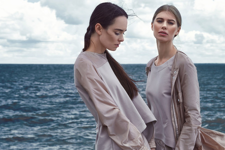 Beautiful sexy woman fashion model brunette and blond style clothes wear silk dress autumn summer collection pose natural makeup accessory storm weather ocean water sea  cloudy sky seaside dramaticの写真素材