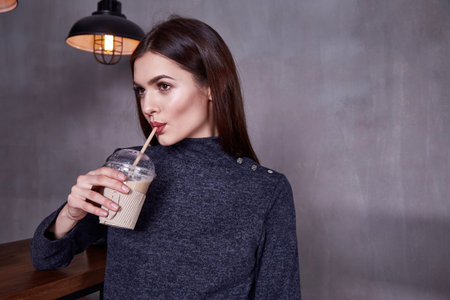 Sexy brunette businesswoman beautiful woman wear stylish clothes catalog fashion in interior room cafe bar accessory organic cotton sweater pants perfect makeup lips drink coffee casual meeting.の写真素材