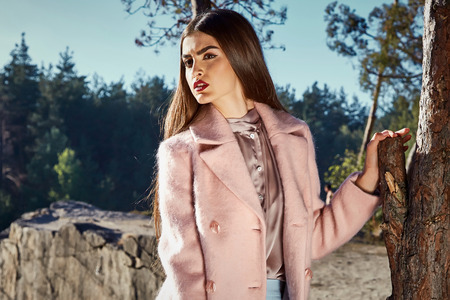 Sexy beautiful woman wear pink color cashmere wool coat blue denim jeans autumn brunette hair fashion catalogue accessory bag in forest park walk tree and lake nature organic sun shine model.の写真素材