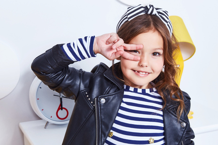 Portrait of small little lady pretty girl cute kid smile hand curly brunette hair wear fashion style clothes for baby strip t-shirt lather jacket hat bow play room for game toy fun party furniture.の写真素材