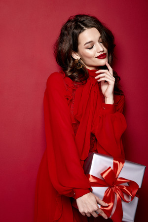 Beautiful young sexy woman thin slim figure evening makeup fashionable stylish dress clothing collection, brunette, gifts boxes red silk bows holiday party birthday New Year Christmas Valentine's Day.の写真素材