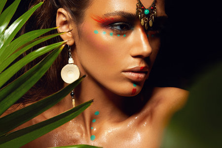 Closeup portrait of woman tanned skin colored makeup tropical jungle paint on the face sweat plant...