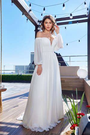 Beautiful tender young woman sexy brunette bride in a luxury white wedding dress lace chiffon Summer happiness awaits the groom before the wedding ceremony makeup accessory jewelry smile.の写真素材