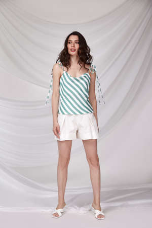 Beautiful sexy woman wear light color short and blouse summer collection cotton casual style tanned body brunette hair beautiful face makeup white background studio.の写真素材