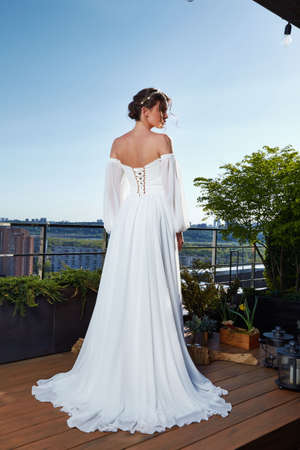 Beautiful tender young woman sexy brunette bride in a luxury white wedding dress lace chiffon Summer happiness awaits the groom before the wedding ceremony makeup accessory jewelry smile.の写真素材