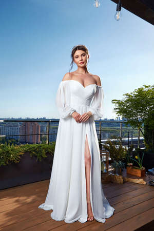 Beautiful tender young woman sexy brunette bride in a luxury white wedding dress lace chiffon Summer happiness awaits the groom before the wedding ceremony makeup accessory jewelry smile.の写真素材