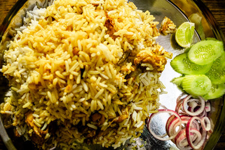 Closeup food photography of Handi Biryani, Asian traditional spicy rice meal served with Chicken, Mutton, Beef and vegetable salad of cucumber, onion, lemon. Popular in Hyderabad, India and Pakistan.の写真素材