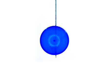Blue natural plastic round plate bottle cap pendulum hanging on stick against isolated white background. Scientific Pendulum is used for hypnotism, reading, swinging, experiment. Copy space for text.の写真素材