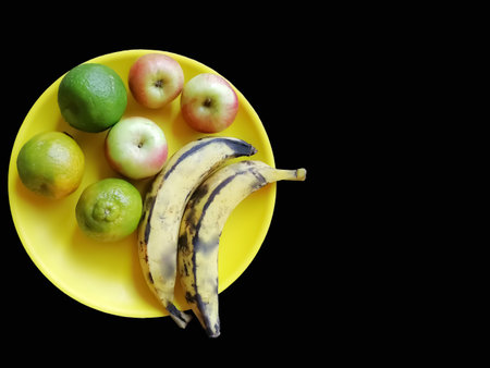 Fruits Bananas Apples and Oranges in an yellow bowl isolated on black backgroundの写真素材