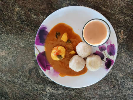 Closeup shot of delicious Kerala style breakfast dish ( Kozhukatta) with egg curry and a glass of tea in a bowl isolated on a surface.の写真素材