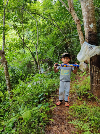Kasaragod,Kerala,Inida- June 13 2021 A cute Indian baby boy holding folded umbrella standing in the green fieldのeditorial素材