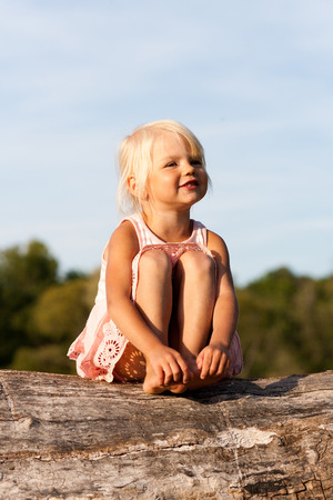 Cute little girl sitting on old treeの写真素材