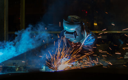 Industrial worker is welding metal part in factory