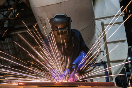 Welder with protective mask welding metal and sparks flying in the air