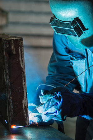 Welder working with arc welding machine to weld steel at factory.